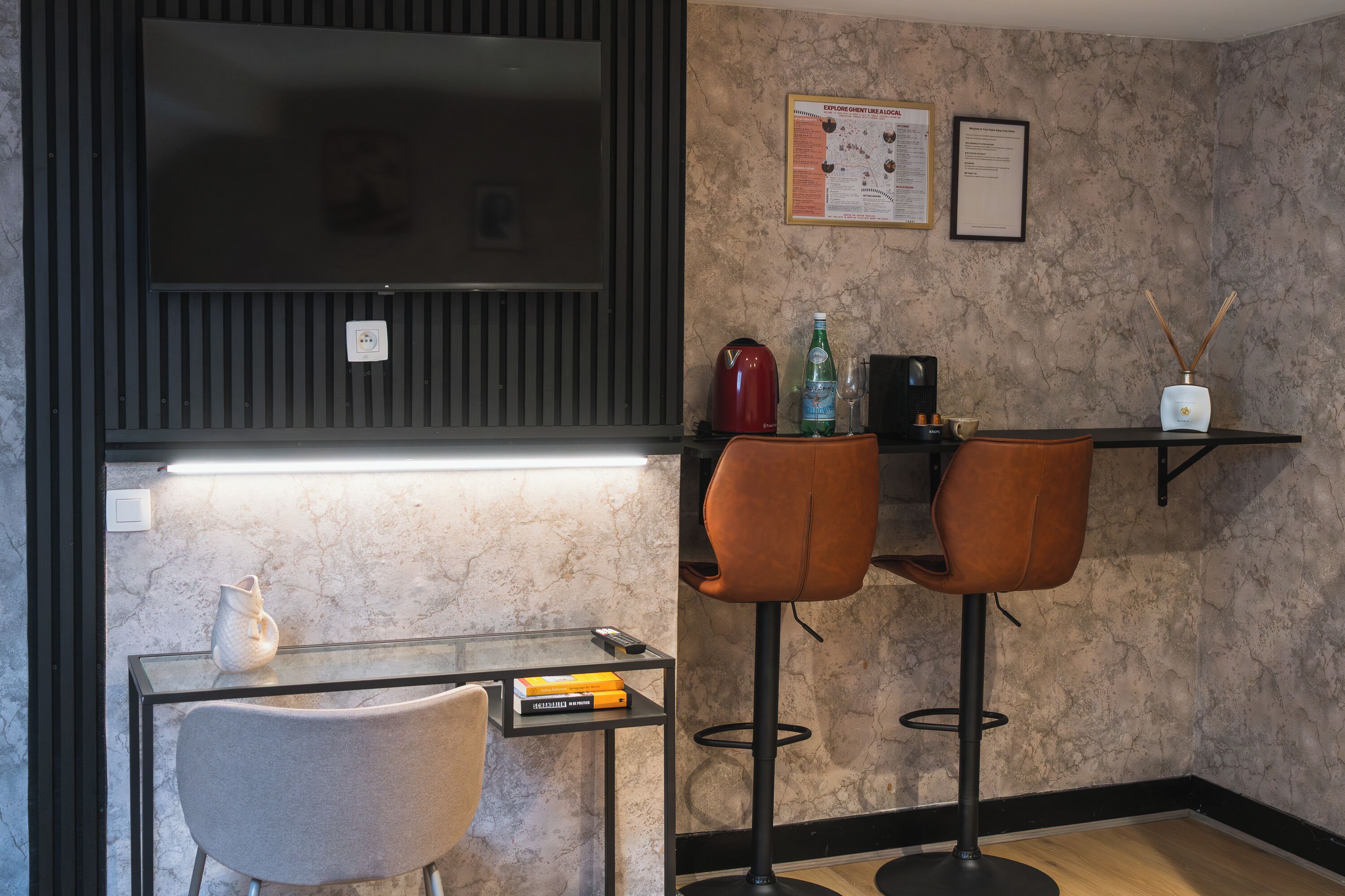 A modern kitchen with a flat-screen TV, a marble backsplash, a small dining table with two chairs, and a coffee machine.