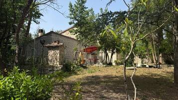 A rustic stone building with a red roof, surrounded by dense greenery and trees.
