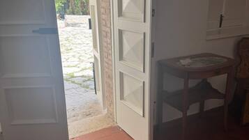 Una habitación con una puerta blanca, una pequeña mesa redonda y vistas a una pared de ladrillo y vegetación exterior.
