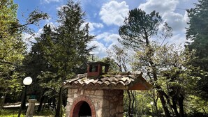 A stone-built outdoor structure with a tiled roof, surrounded by trees and a clear sky. - Daphne Estate (Aia Vecchia)