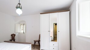 A bedroom with a bed, a wardrobe, a chair, and a hanging light fixture. - Daphne Estate (Aia Vecchia)