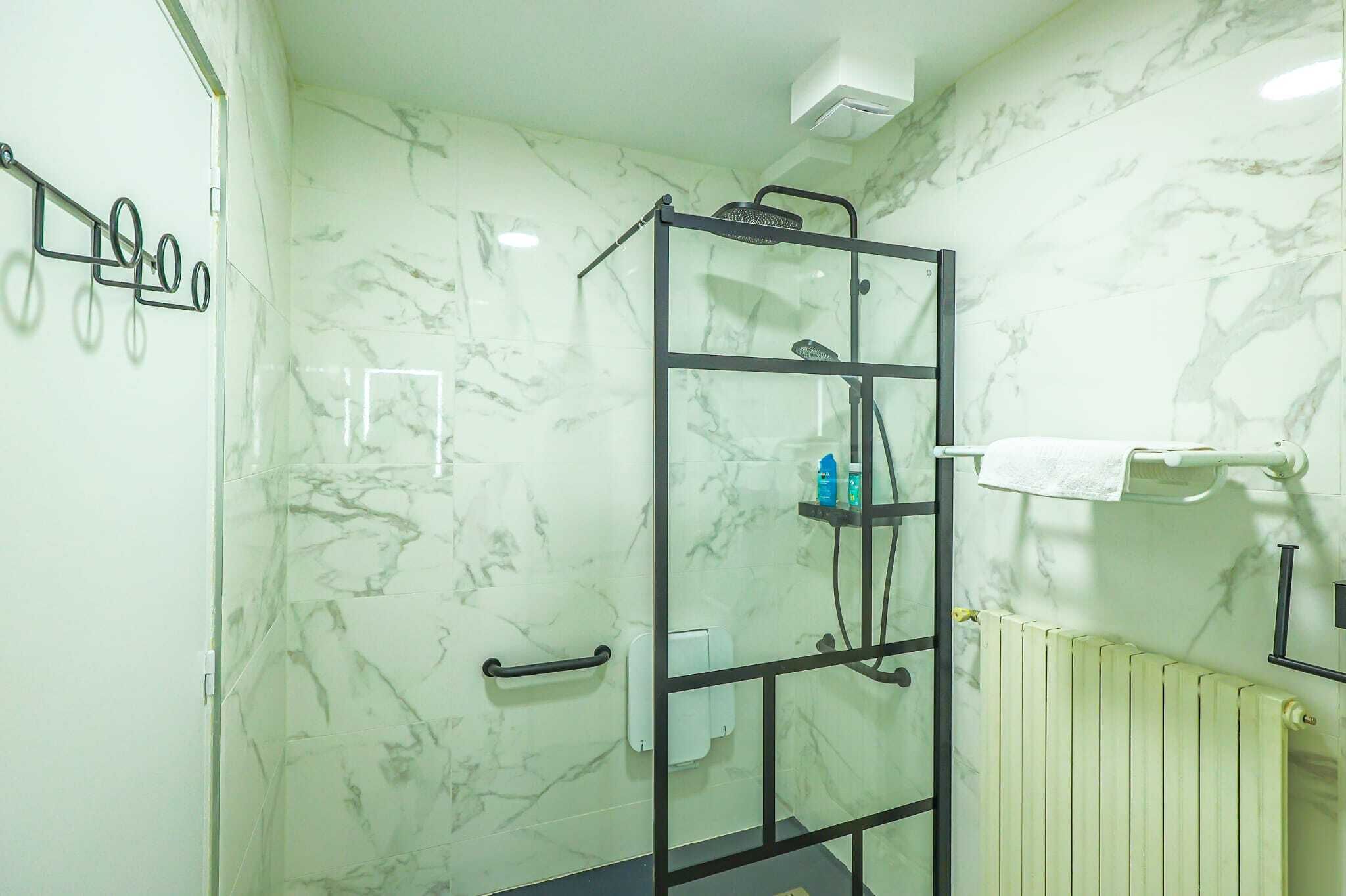 Un baño con cabina de ducha de vidrio, paredes de mármol, un perchero y un radiador.