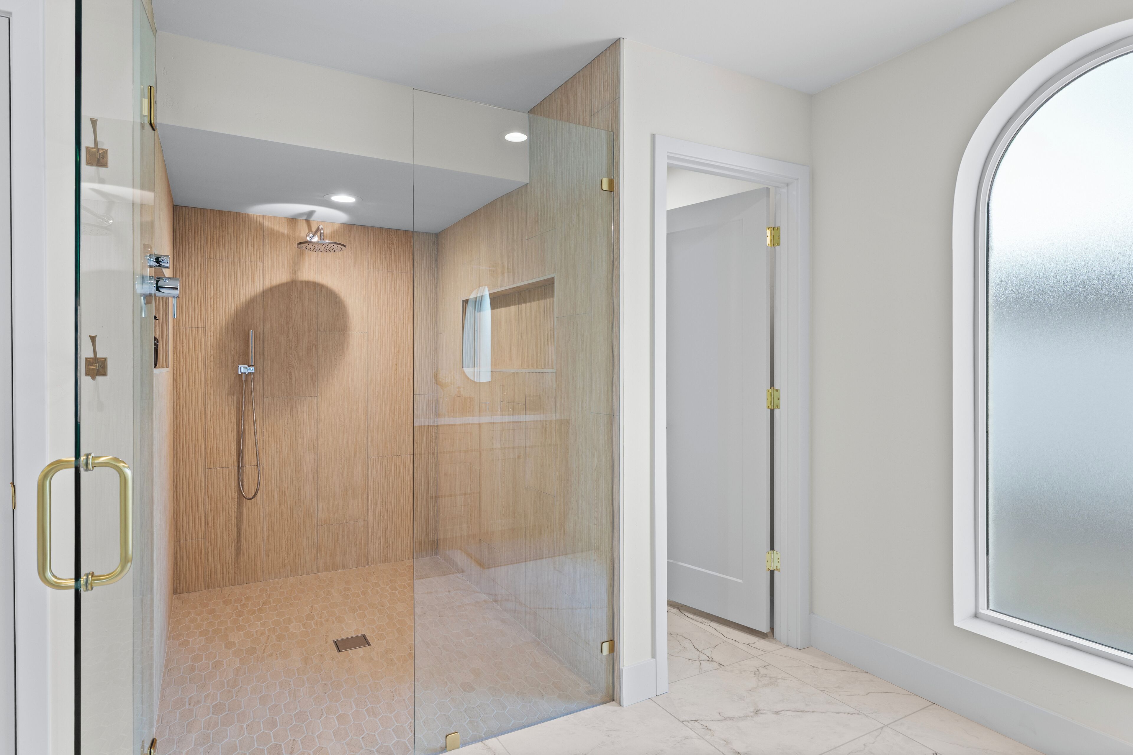 A modern bathroom with a glass-enclosed shower, a wooden vanity, and a large window.