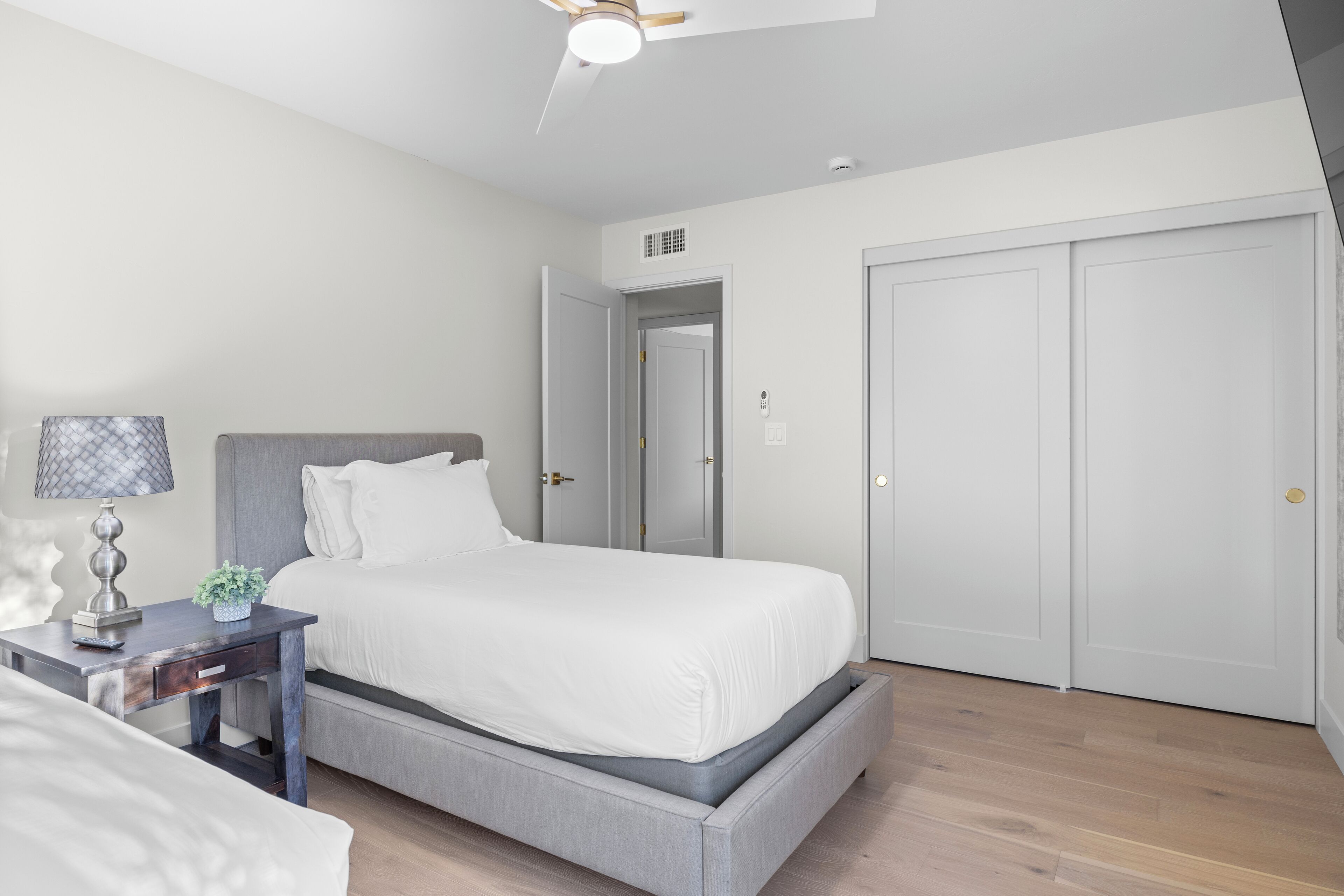 A modern bedroom with a bed, bedside table, lamp, and a door leading to another room.