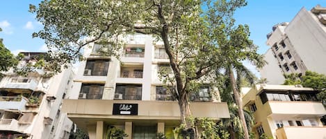 Un edificio de varios pisos con balcones, un letrero y follaje circundante.