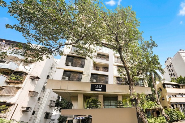 A multi-story building with balconies, a sign indicating a company service, and a tree in the foreground.