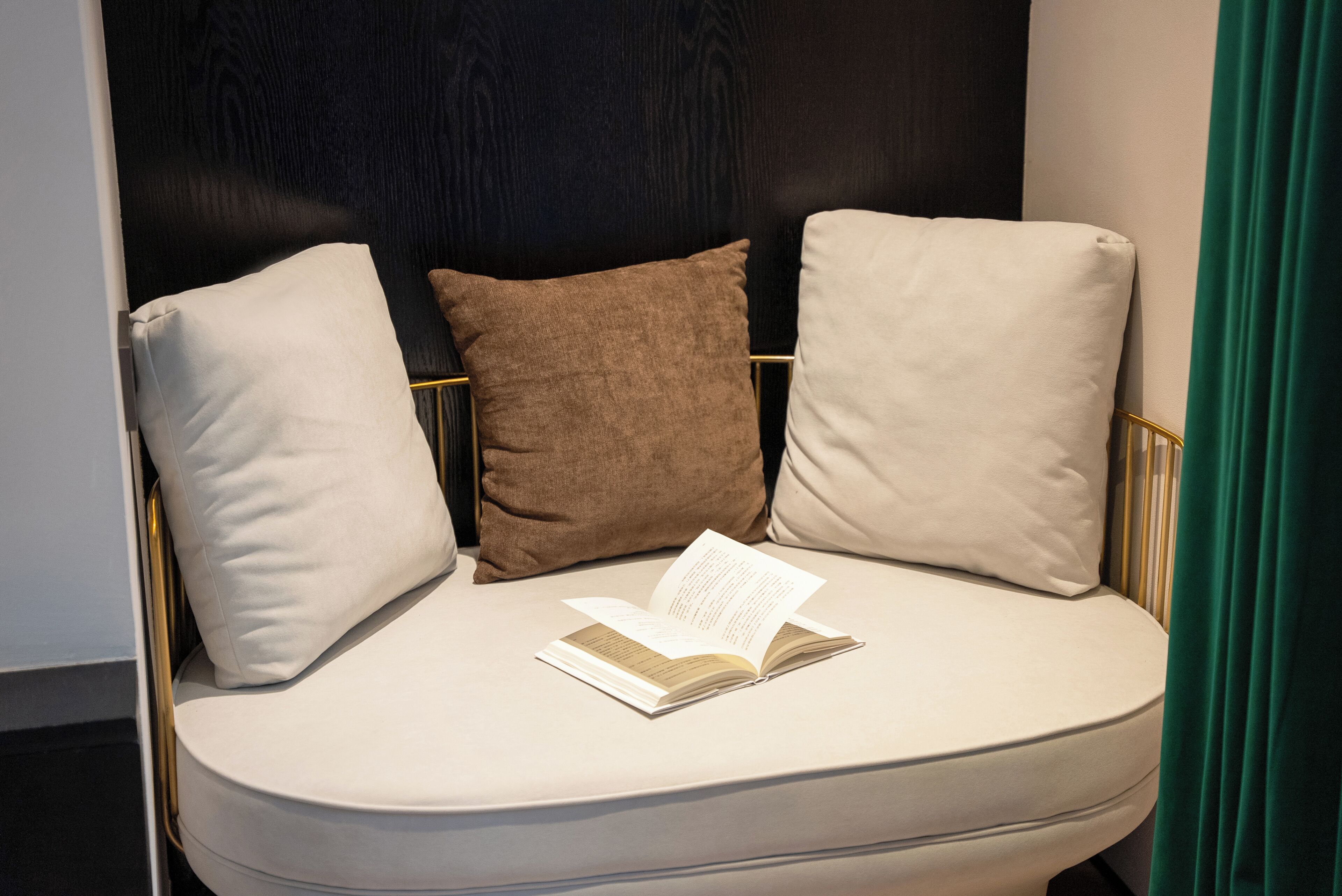 A modern, curved sofa with three cushions in a neutral color palette, positioned against a dark wall with a gold frame.