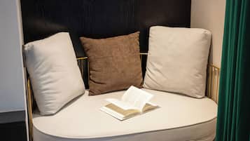 A modern, curved sofa with three cushions in a neutral color palette, positioned against a dark wall with a gold frame.