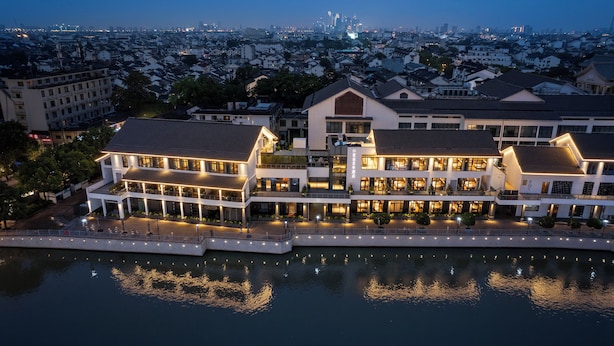 A waterfront hotel with multiple buildings, a dock, and a cityscape in the background. - SSAW Garden Hotel Suzhou (Suzhou)