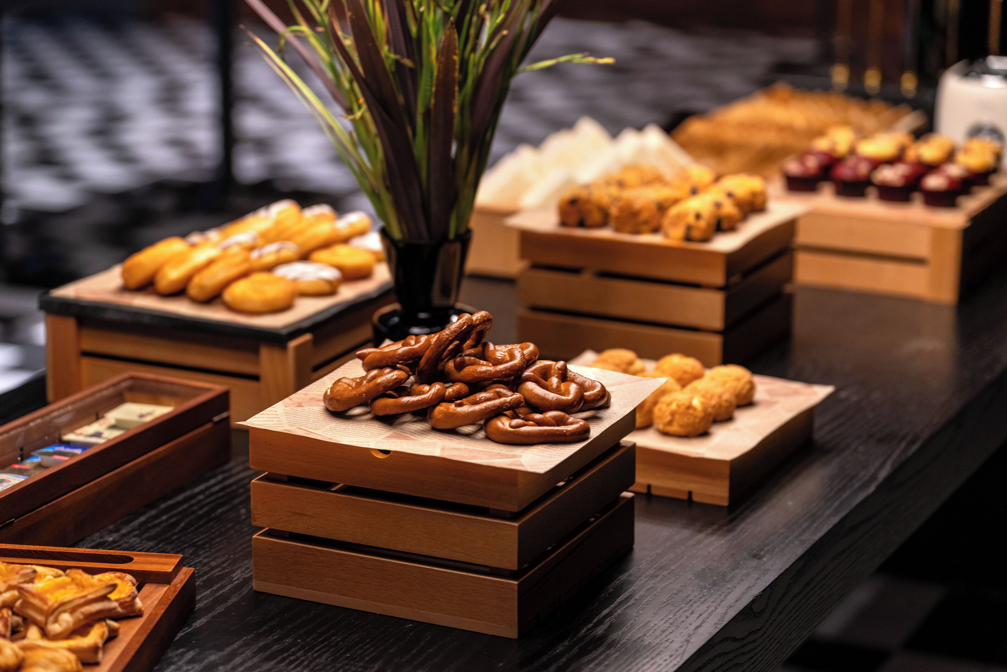 Un tavolo da buffet con diversi prodotti da forno, tra cui pretzel e pasticcini, disposti in scatole di legno.