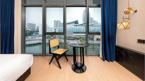 A hotel room with a bed, a chair, a small table, and a view of a cityscape through large windows. - SSAW Garden Hotel Suzhou (Suzhou)