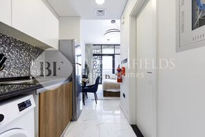 A modern kitchen with a marble countertop, a built-in washing machine, and a dining area with a blue chair.