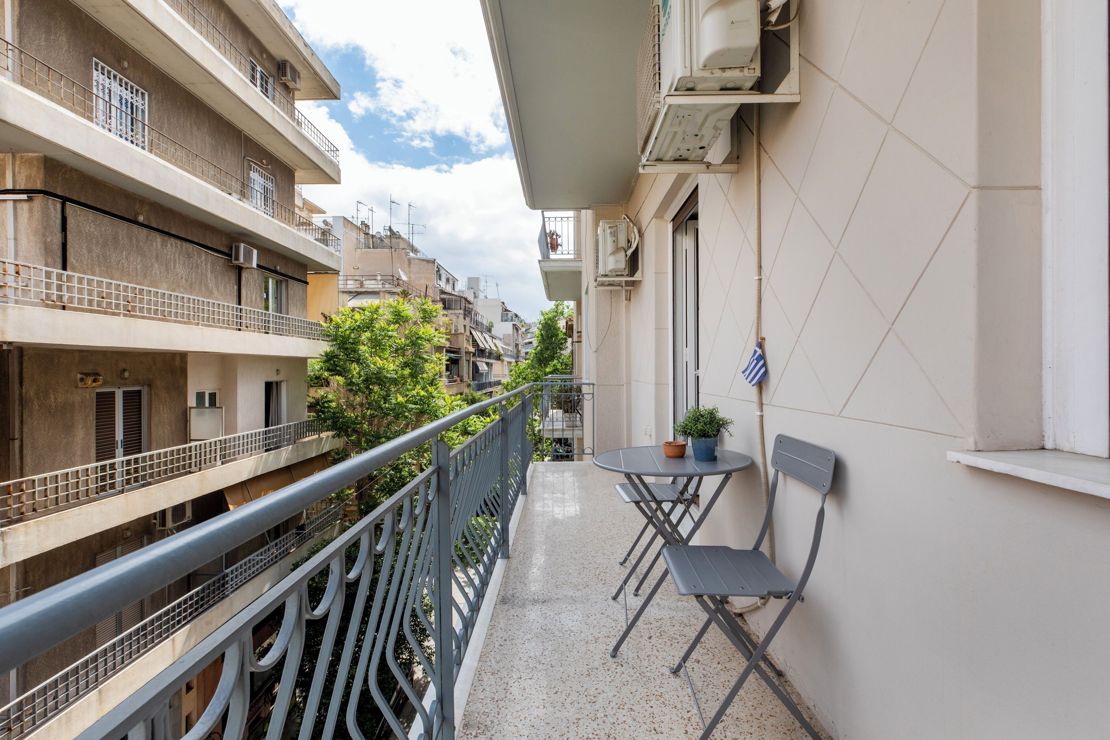 A balcony with a table and chairs, a potted plant, and a view of neighboring buildings.
