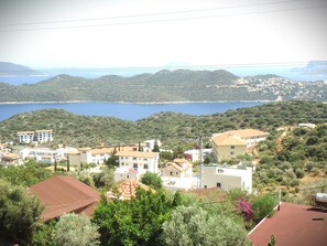 A coastal town with buildings, a view of the sea, and hills in the background. - HAYAT PANSİYON (Kas)