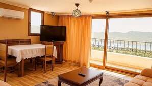 Una habitación con una mesa de comedor, sillas, un televisor, un sofá y un balcón con vistas a las montañas.