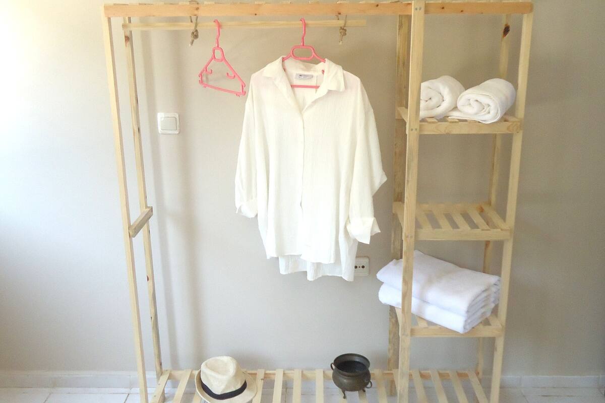 A wooden wardrobe with a white shirt hanging on a pink hanger, a hat, and a small pot on the lower shelf.