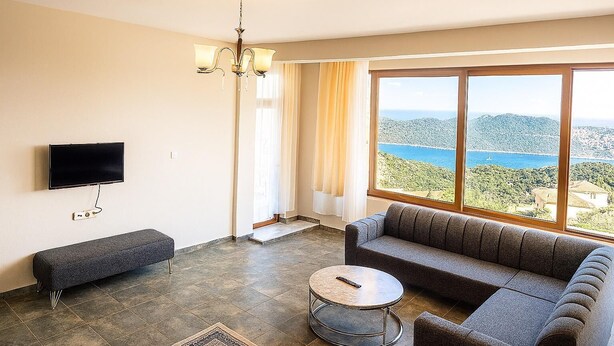 Una sala de estar con sofá, una mesa redonda de centro, televisor montado en la pared y un amplio ventanal con vistas panorámicas.
