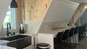 Une cuisine moderne avec un plafond en pente, des murs en bois, un plan de travail blanc et des tabourets de bar noirs.