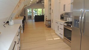 Une cuisine moderne avec un plancher en bois, des armoires blanches, des appareils électroménagers en acier inoxydable et un escalier apparent menant à l’étage supérieur.