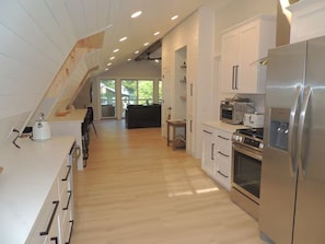 Una cocina moderna con suelo de madera, armarios blancos, electrodomésticos de acero inoxidable y una escalera visible que conduce a un nivel superior.