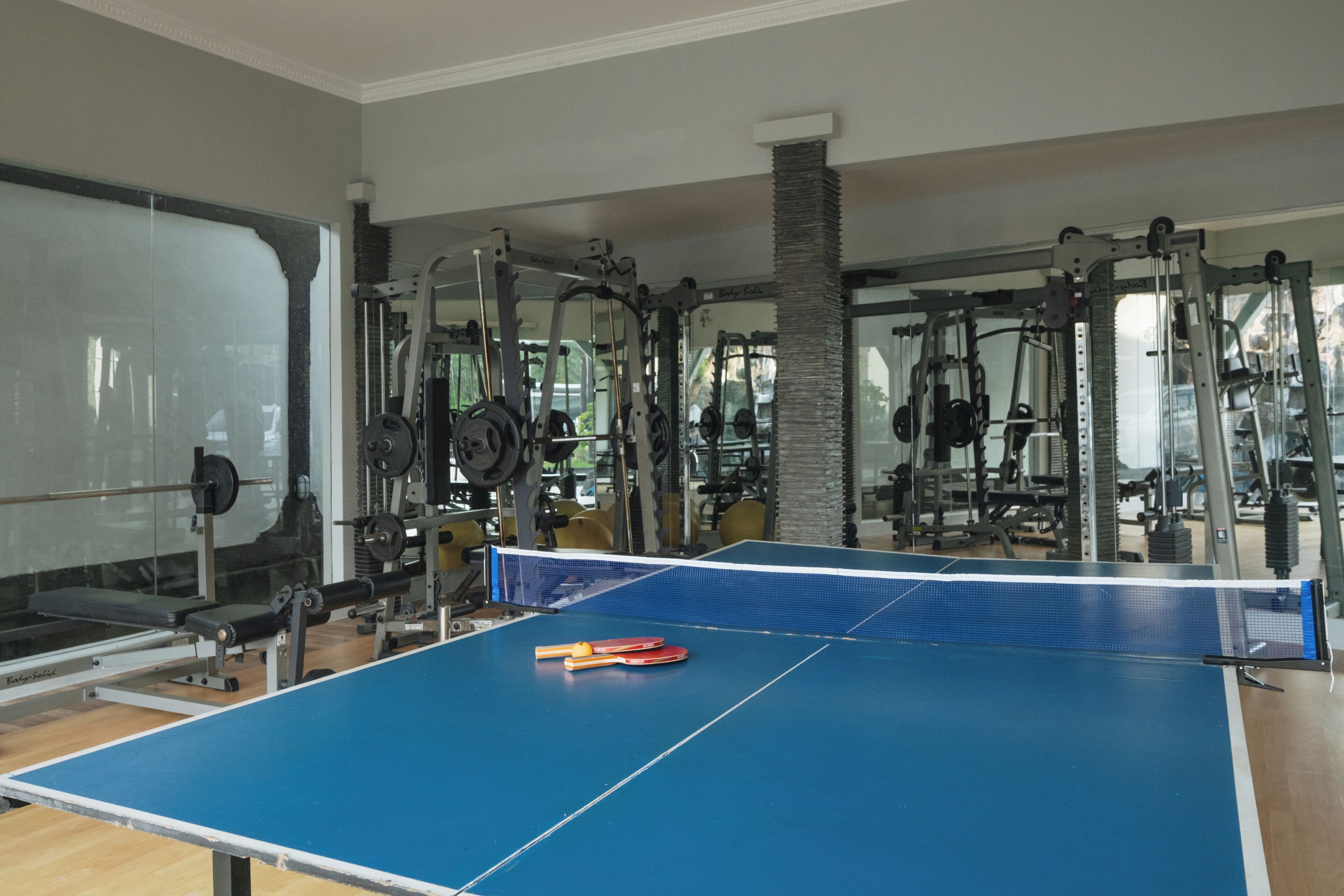 A gym with a ping pong table, weightlifting equipment, and a large mirror.