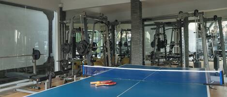 A gym with a ping pong table, weightlifting equipment, and a large mirror.
