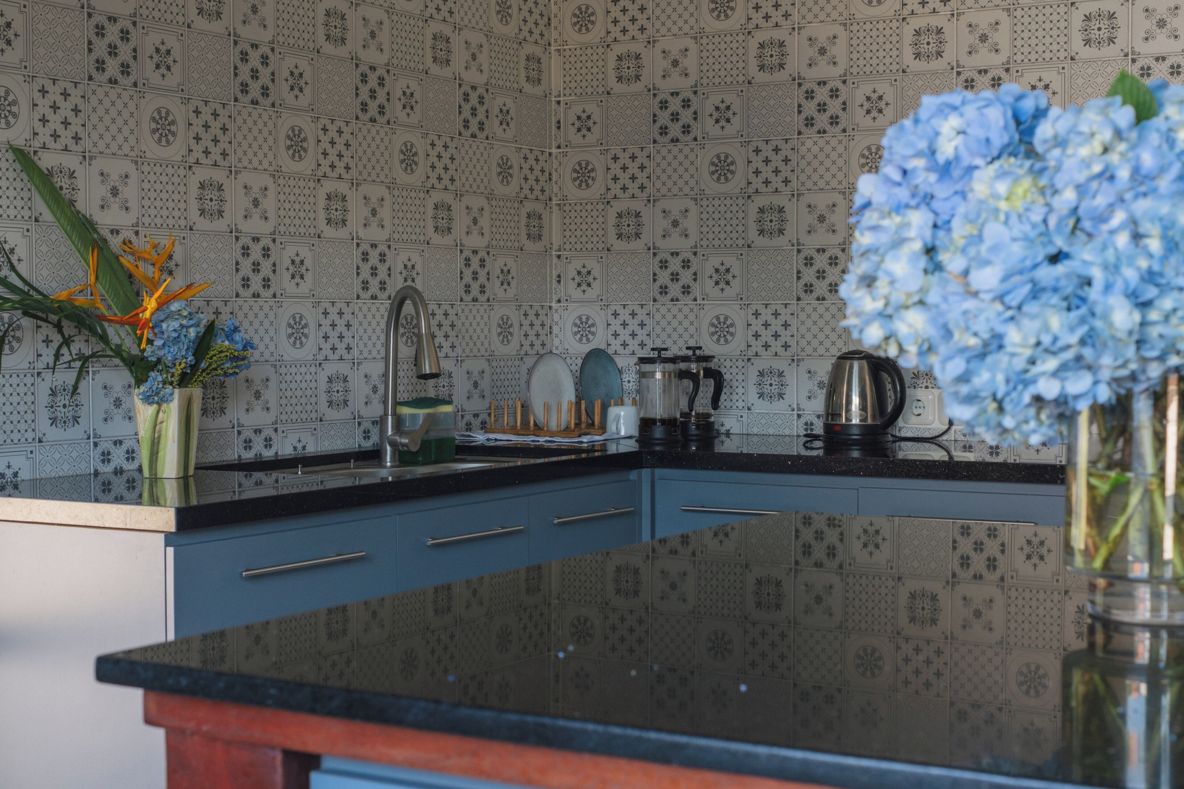 A kitchen with patterned tiles, a black countertop, and a vase with flowers.