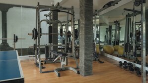 Un gimnasio con equipamiento de levantamiento de pesas, un espejo grande y una mesa de ping pong.