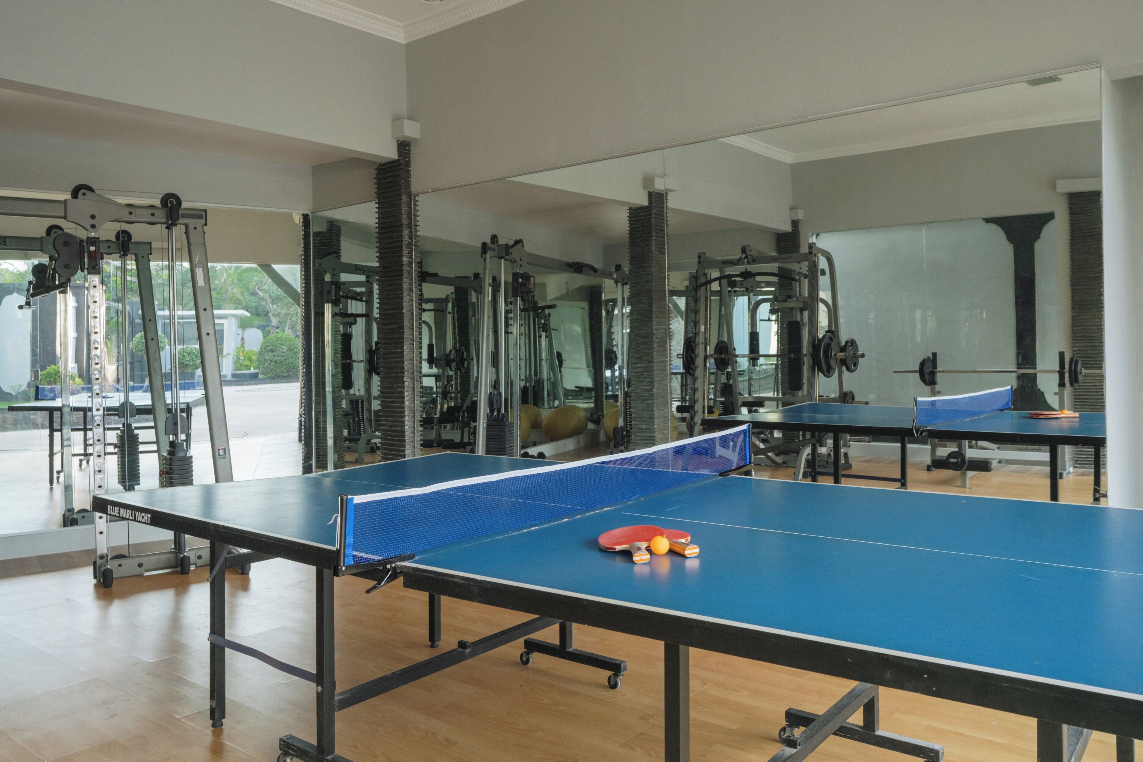 Un gimnasio con mesa de ping pong, equipo de ejercicio y espejos grandes.