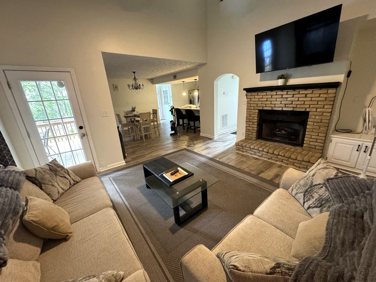 A living room with a fireplace, a television mounted above it, and a dining area in the background.