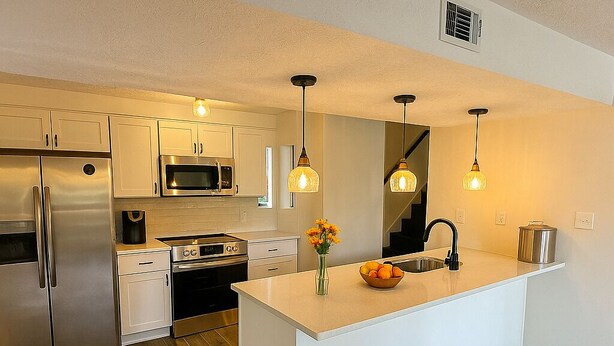 A modern kitchen with stainless steel appliances, a central island, pendant lighting, and a wooden floor.