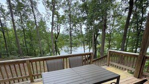 A wooden deck with a table and chairs, overlooking a lake surrounded by trees.