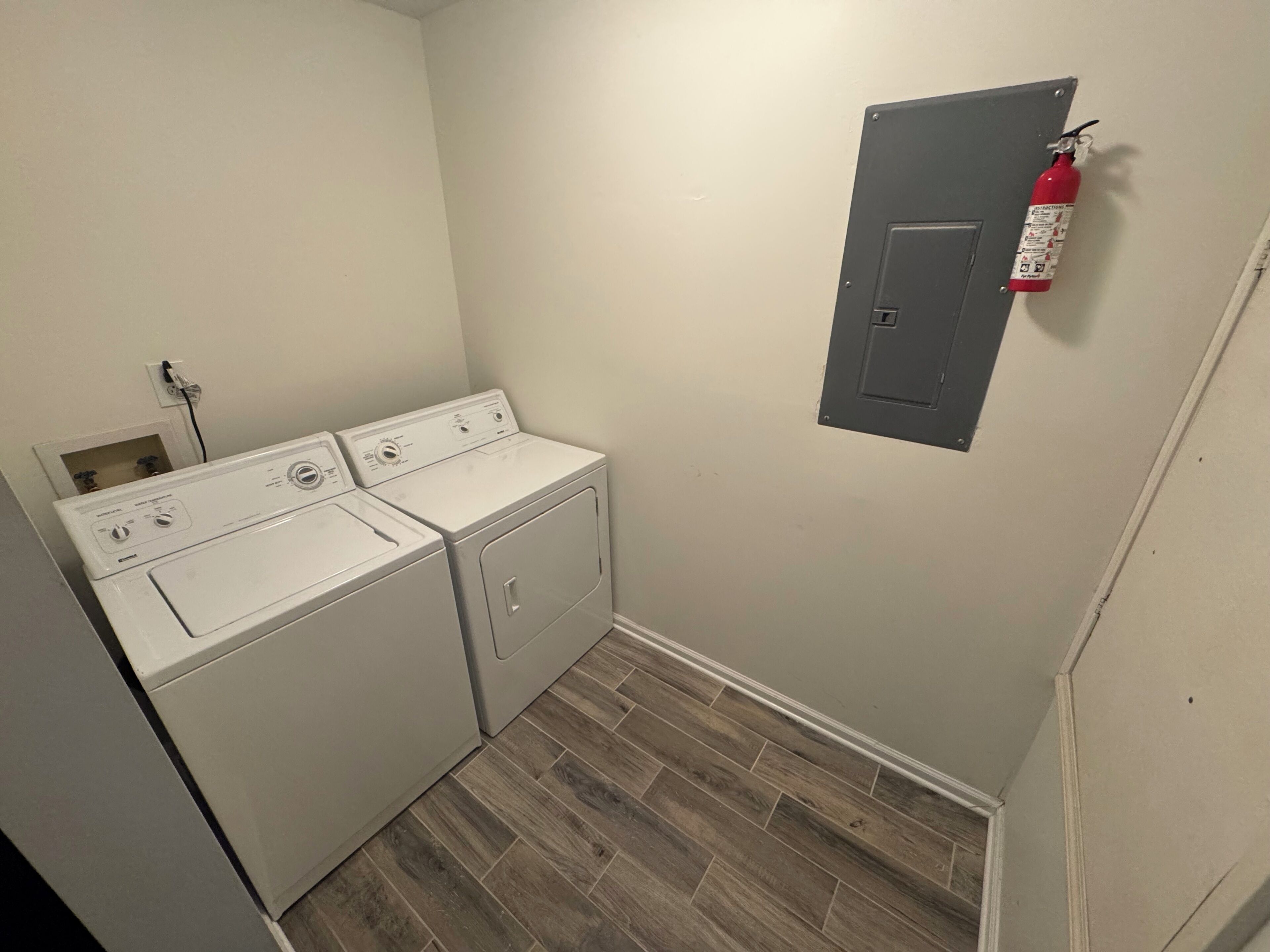 Une buanderie équipée de deux machines à laver et deux sèche-linge blancs, d’un extincteur fixé au mur et d’un plancher en bois.