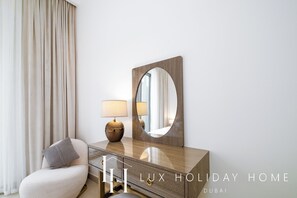 Une chambre d’hôtel moderne avec une coiffeuse en bois, un miroir rond, une lampe et un fauteuil confortable.