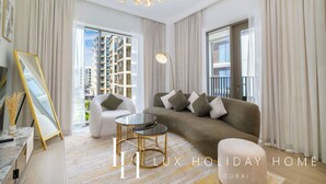Un salon spacieux comprenant un canapé, des fauteuils et une table basse. Il y a une grande fenêtre avec des rideaux, un lustre et une vue sur des immeubles de grande hauteur.
