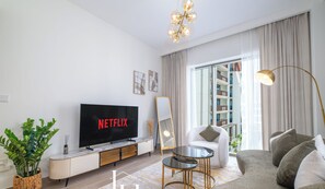 Een moderne woonkamer met een flatscreen-televisie waarop 'NETFLIX' wordt weergegeven, een bank, een salontafel en een groot raam met gordijnen.