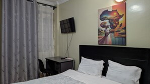 A hotel room with a bed, a desk, a chair, a TV, and a painting on the wall. - Live Light, Live Right.Fully-Furnished Studio Apartment in Machakos! (Machakos)