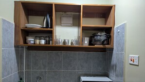 A kitchen with a sink, a microwave, and a shelf with kitchenware. - Live Light, Live Right.Fully-Furnished Studio Apartment in Machakos! (Machakos)