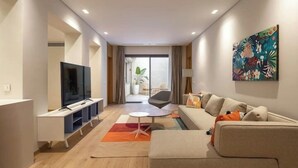Una sala de estar moderna con un televisor de pantalla plana, un sofá, una mesita de centro y un cuadro abstracto colorido en la pared.