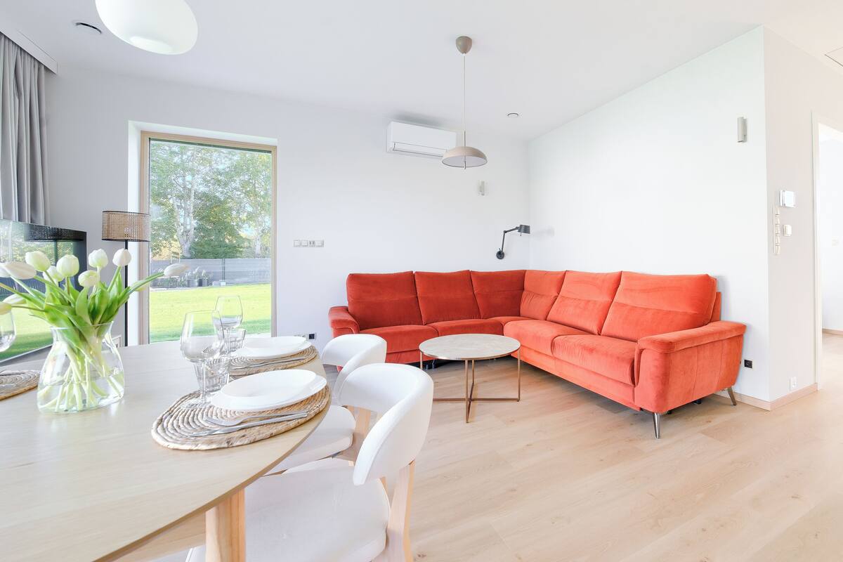 A modern living room with a red sectional sofa, a round coffee table, and a dining area with a wooden table and white chairs.