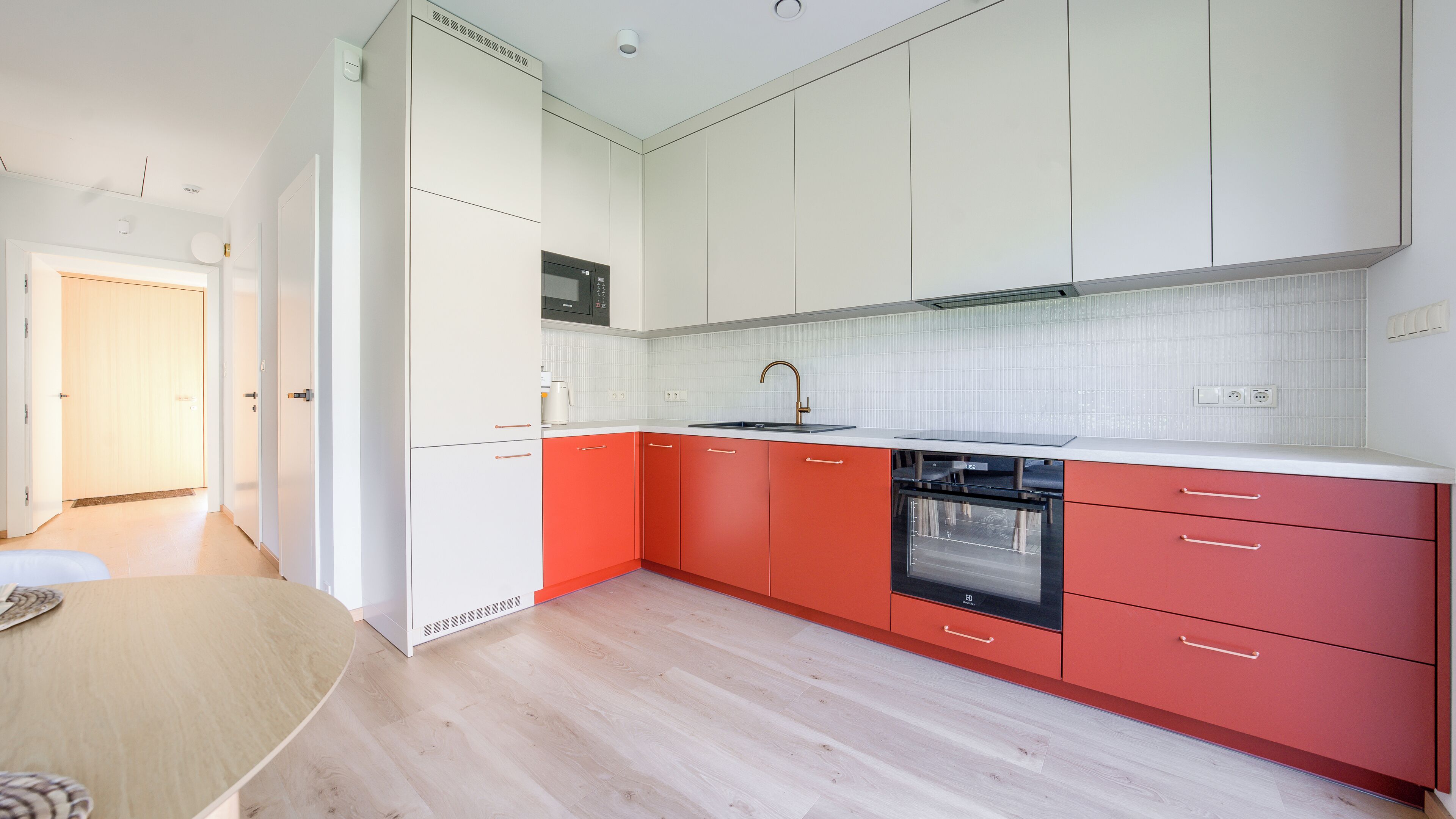 Une cuisine moderne avec des meubles blancs et rouges, un évier en acier inoxydable et un four encastré.