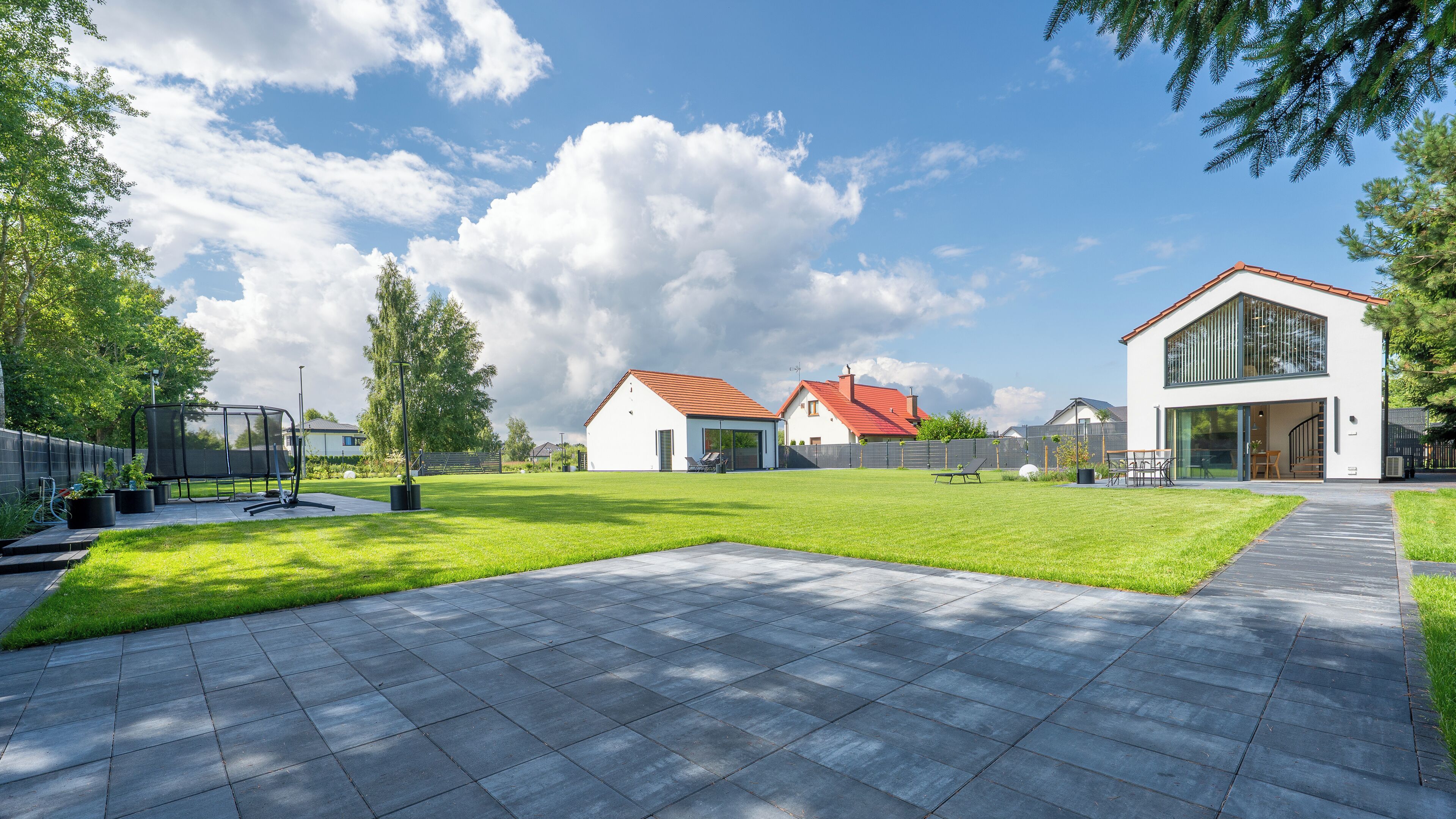 A modern residential area with a well-maintained lawn, paved pathways, and contemporary houses with red roofs.
