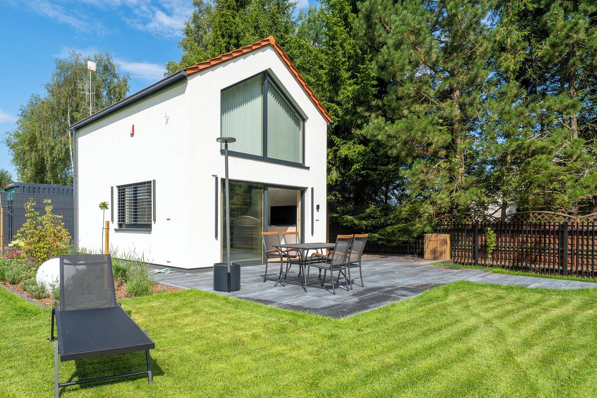 A modern two-story house with a patio, outdoor seating, and a well-maintained lawn.