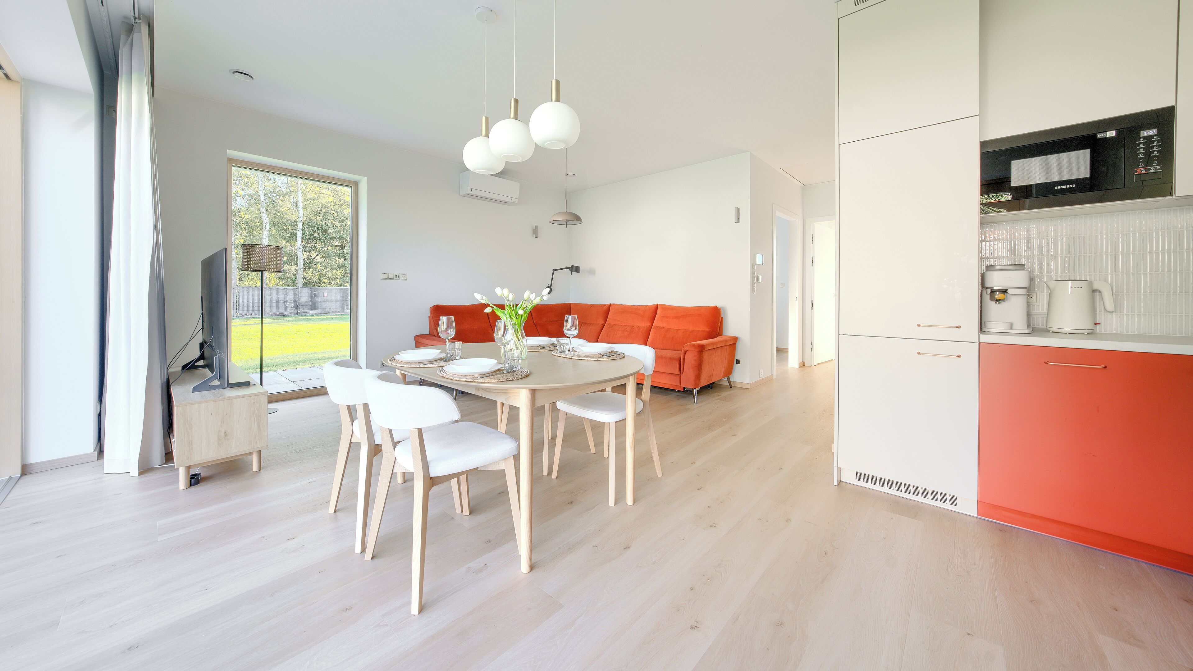 Ein moderner Essbereich mit einem runden Tisch, weißen Stühlen und einer roten Couch im Hintergrund.