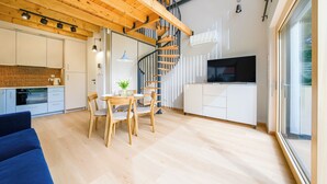 A modern kitchen with a wooden staircase, a dining area with a table and chairs, and a large window providing natural light. - Inteligentne Rubinowe Domy Sun & Snow (Grzybowo)