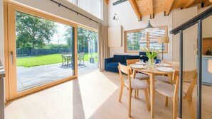 A modern interior with a dining area, a blue sofa, and a large sliding glass door leading to a garden. - Inteligentne Rubinowe Domy Sun & Snow (Grzybowo)