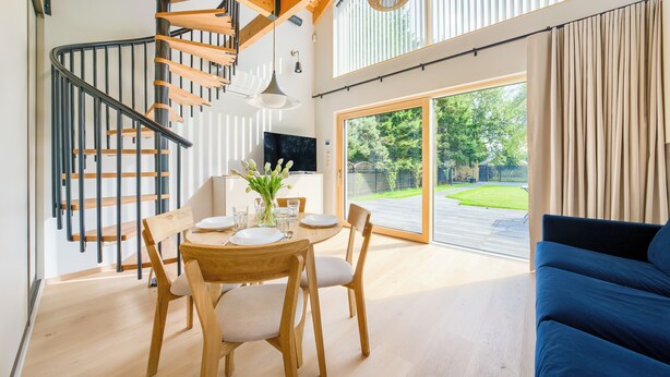 A modern interior with a wooden dining table set for four, a blue sofa, and a spiral staircase. - Inteligentne Rubinowe Domy Sun & Snow (Grzybowo)