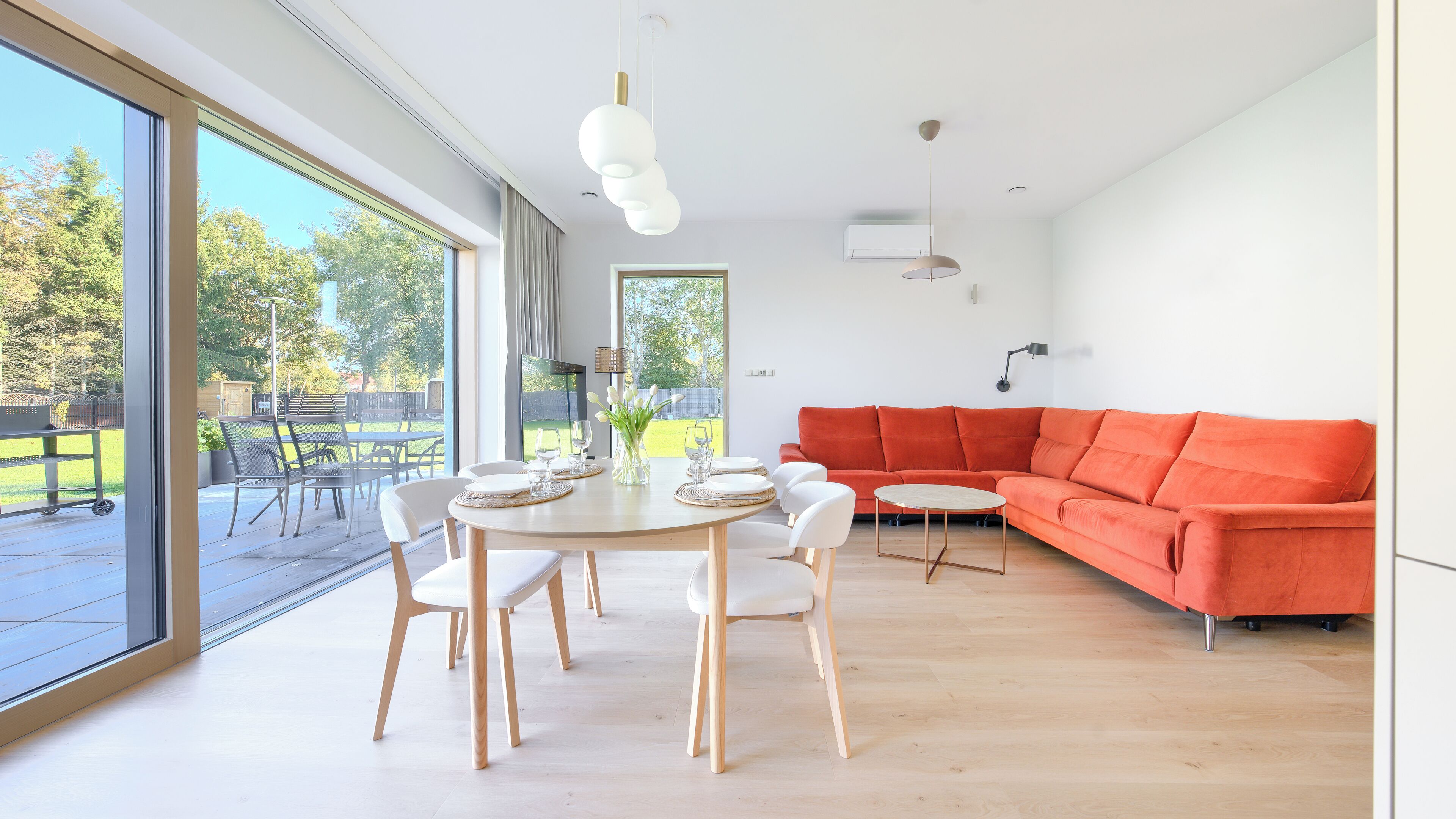 A modern living room with a large window, a dining table with chairs, and a bright orange sofa.