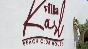 A white wall with the text 'Villa Karl Beach Club House' in red lettering.