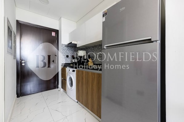A modern kitchen with a stainless steel refrigerator, a washing machine, and wooden cabinets. - Bloomfields Homey Stu The Gate Masdar  (Abu Dhabi)